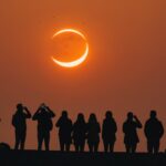 Éclipse solaire partielle en forme de croissant dans un ciel orange au-dessus d'une skyline européenne